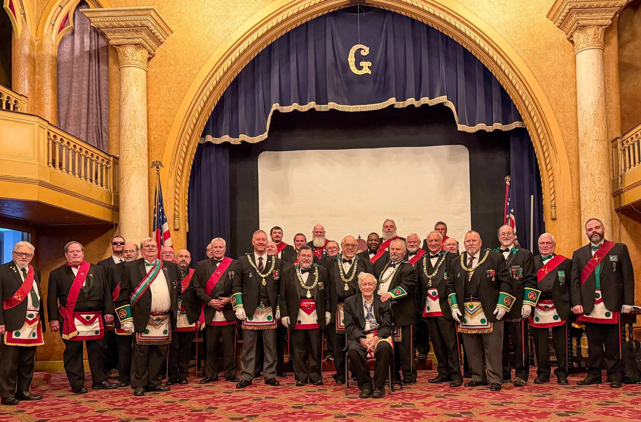 Sir Knights assembled before an ornate stage in a historic hall.